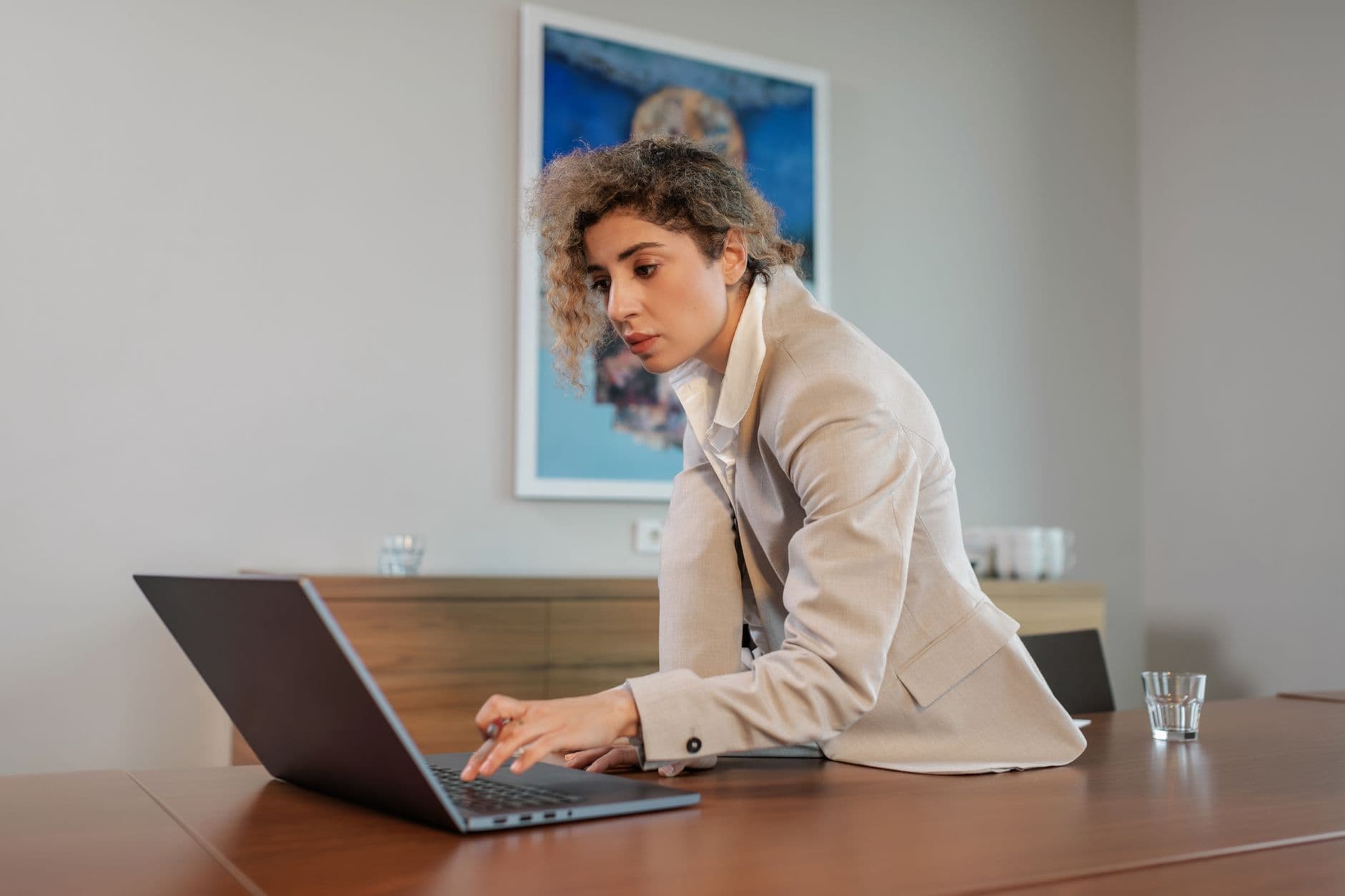 Businesswoman in a beige blazer working on a laptop at a modern office desk.